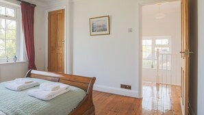 Ein Schlafzimmer mit einem hölzernen Bett, einem Fenster mit Vorhängen, einer Tür und einem Bild an der Wand.
