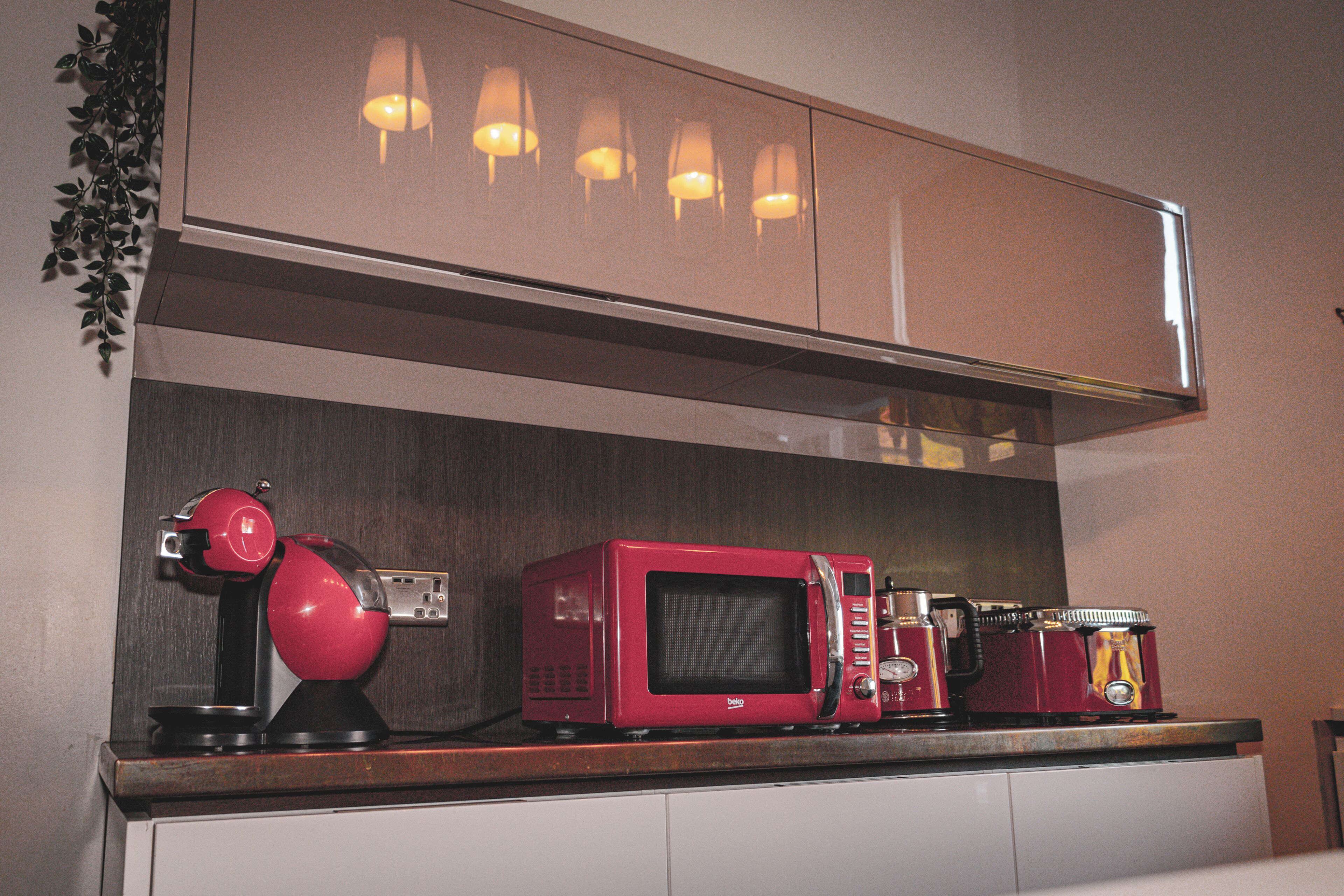 Una cocina con microondas, un electrodoméstico rojo y una cafetera sobre la encimera.
