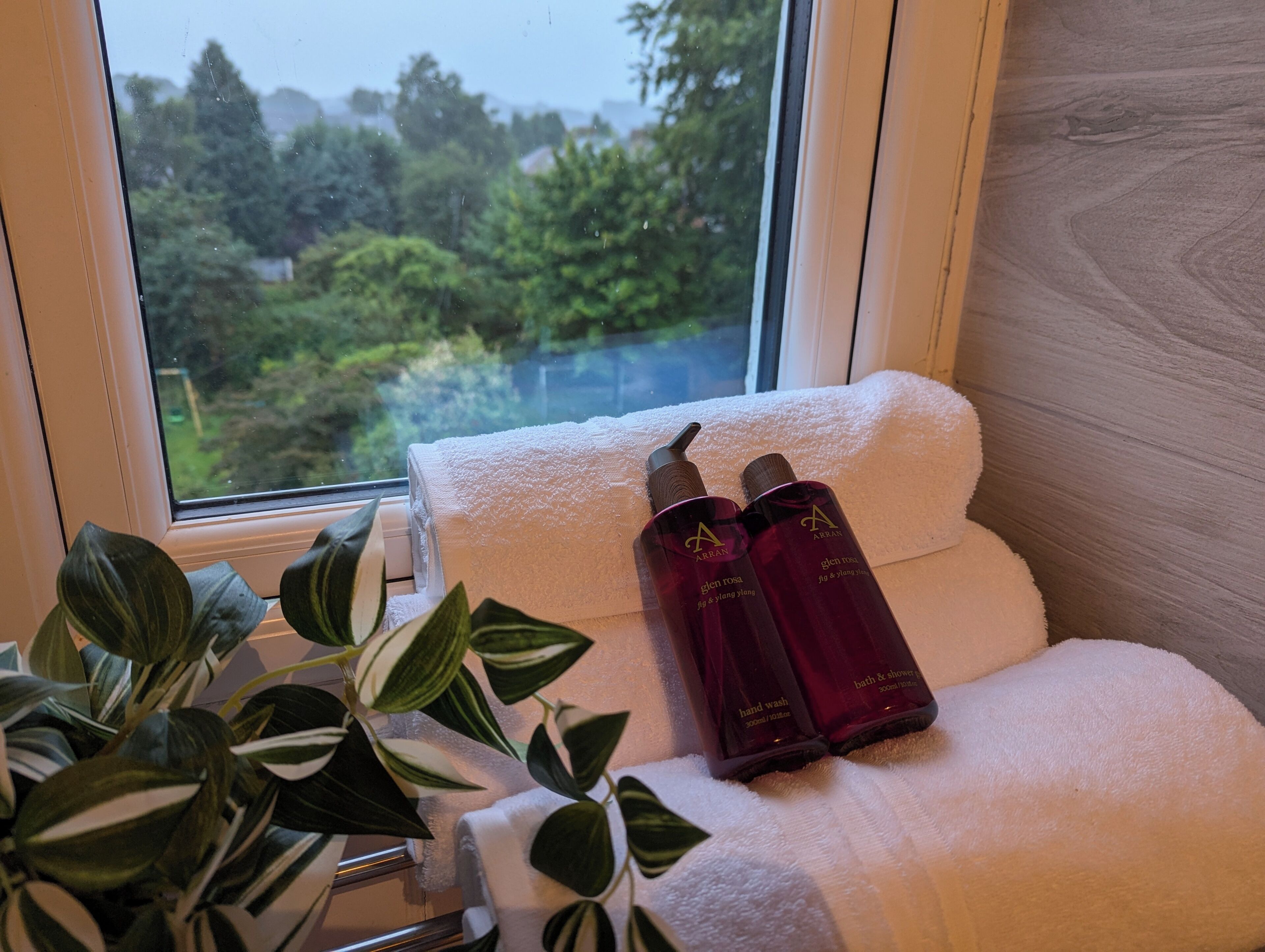 A bathroom with a window view of greenery, a white towel, and two bottles of bath products.