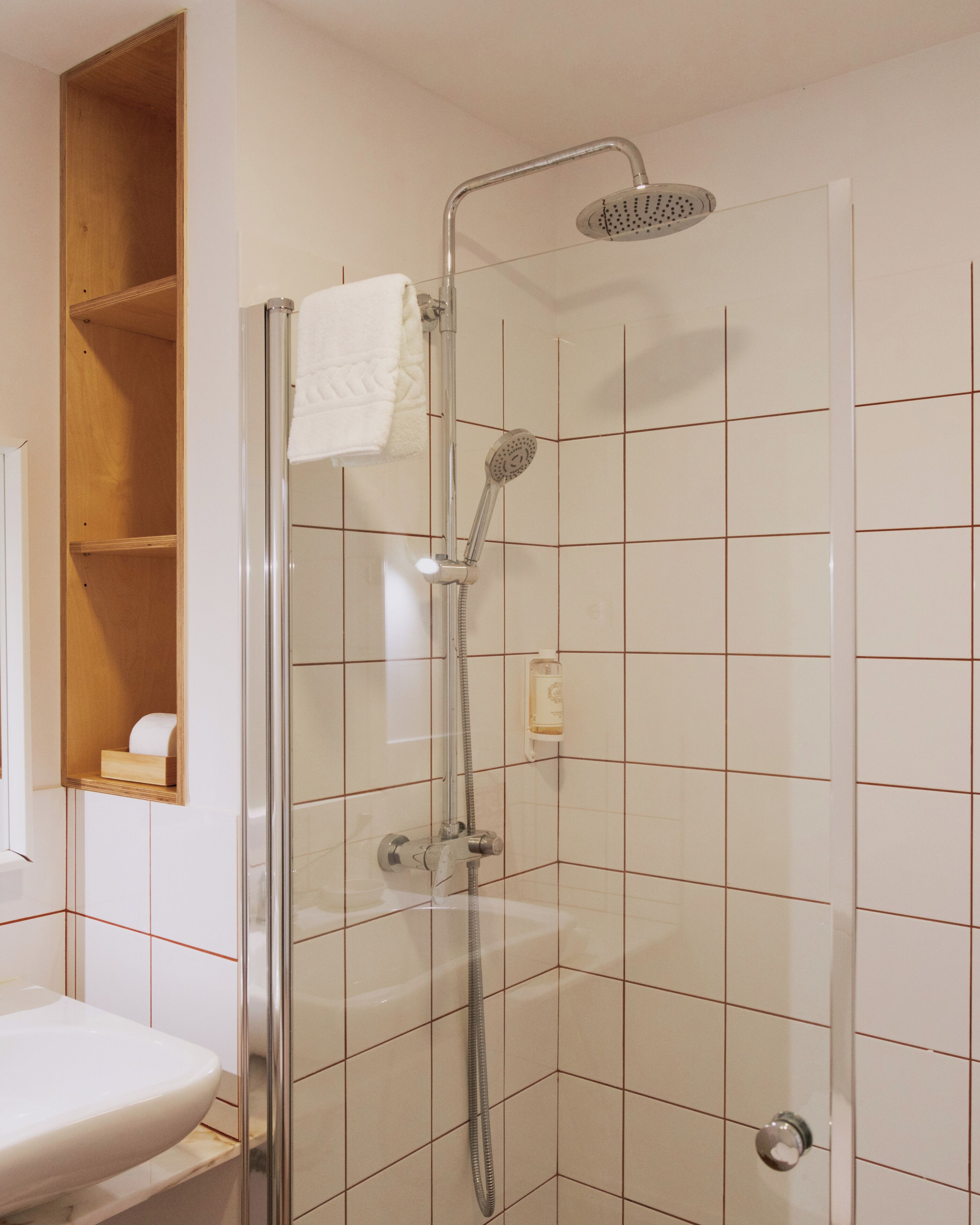 A glass-enclosed shower with a handheld showerhead and a wall-mounted faucet.