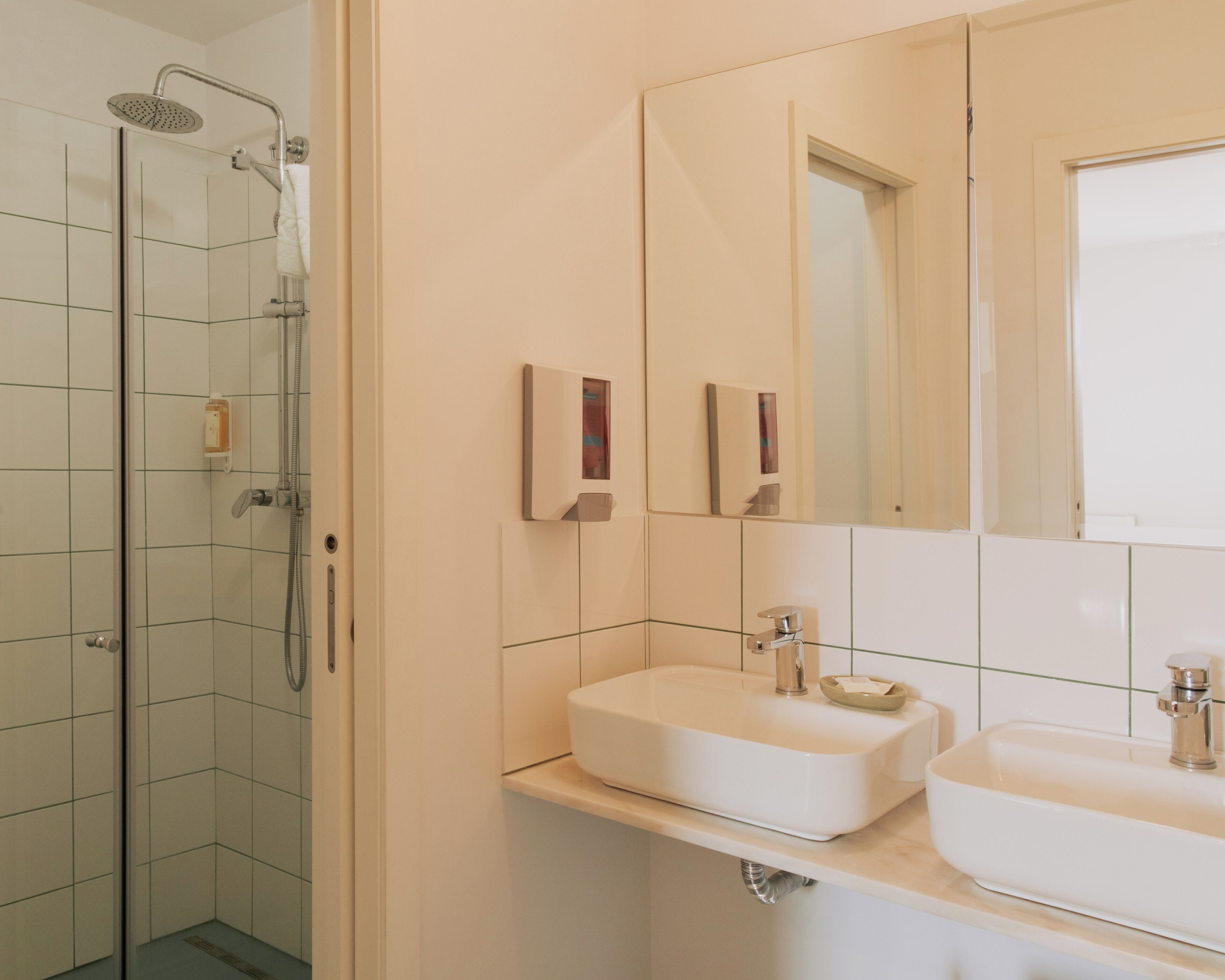 Ein Badezimmer mit einer gläsernen Duschkabine, zwei Waschbecken und einem großen Spiegel.