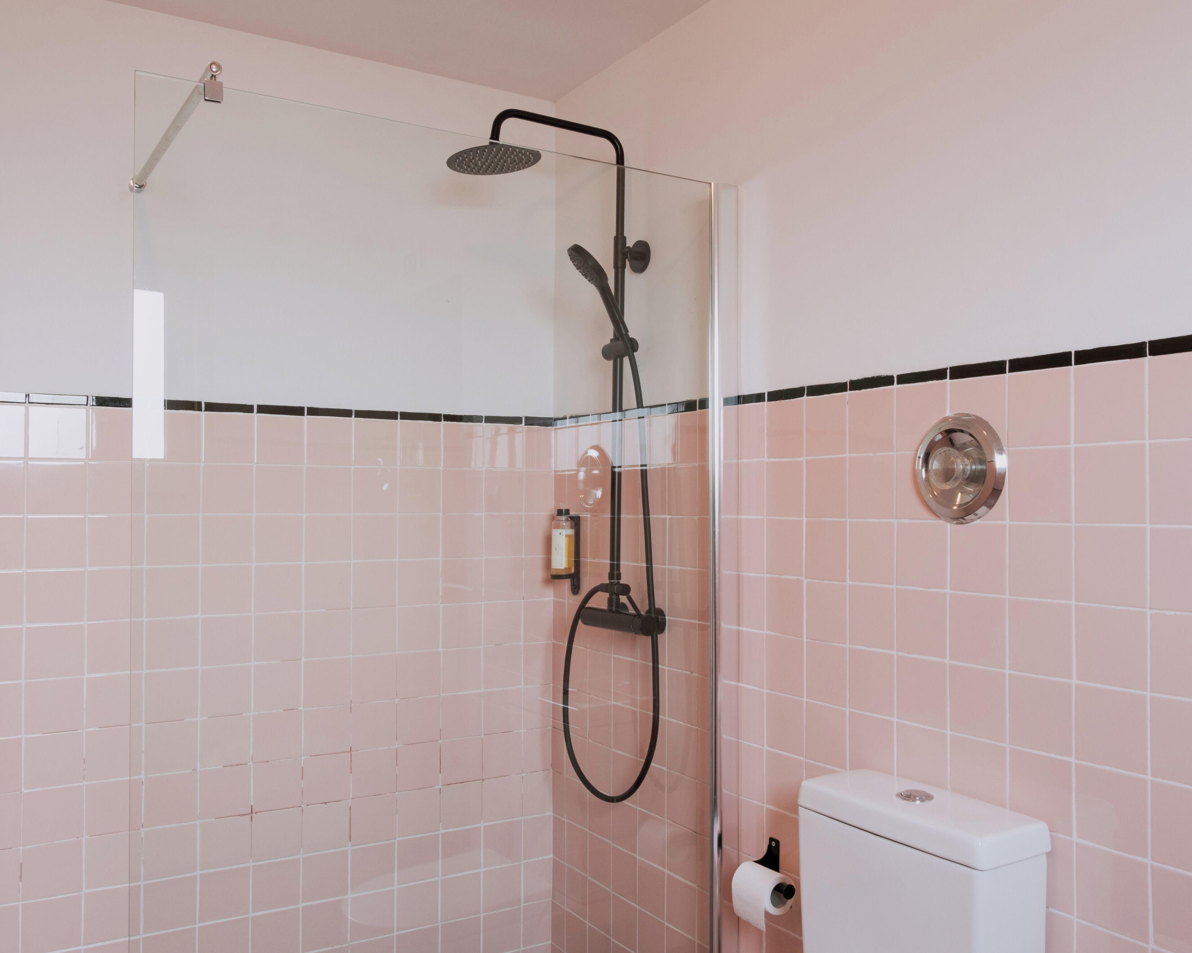 Un baño con cabina de ducha de vidrio, inodoro y dispensador de jabón en la pared.