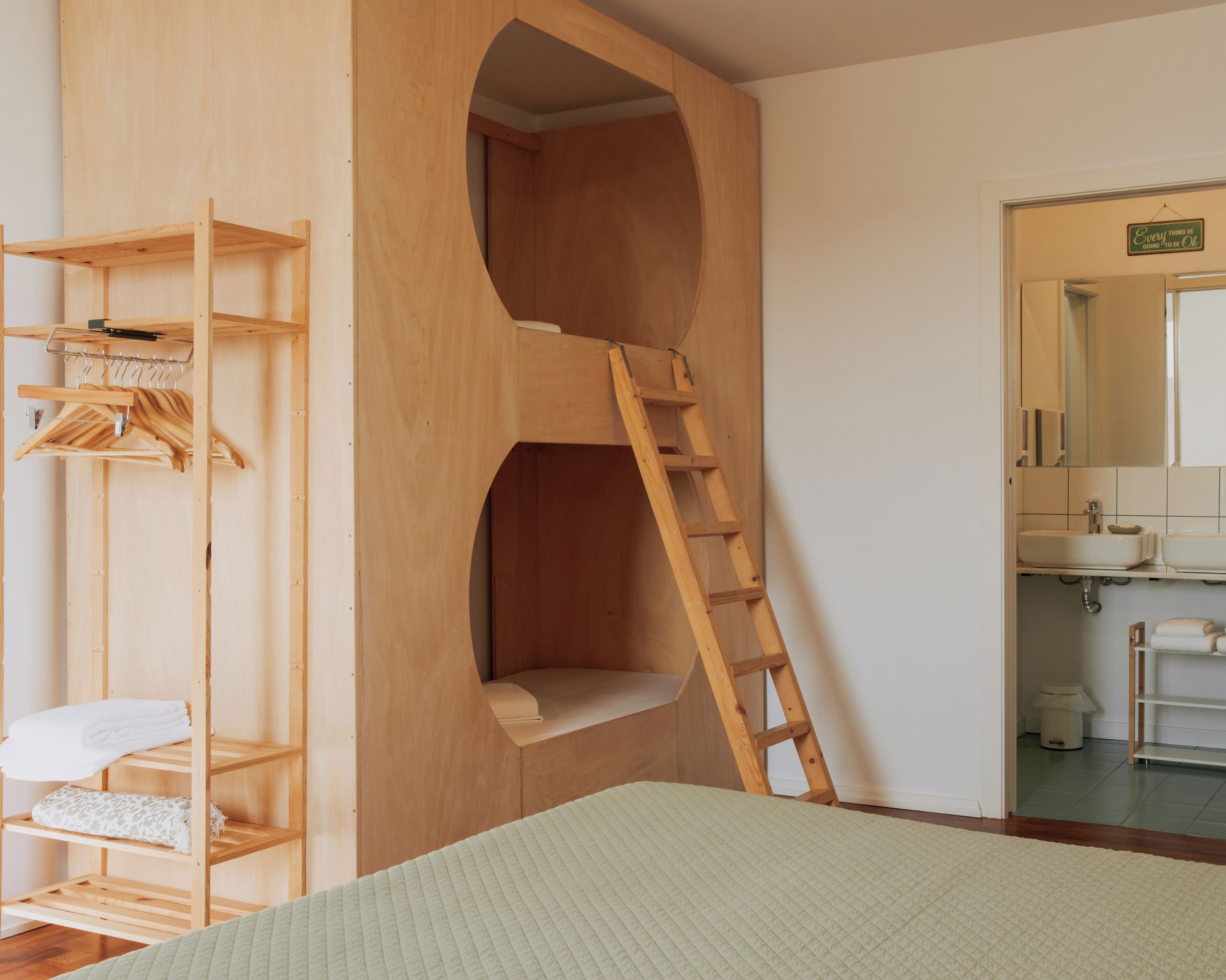 A bedroom with a bunk bed, wooden shelving unit, and a ladder leading to a loft.