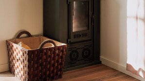 A corner room with a wood-burning stove, a woven basket, and a window with curtains. - Quinta da Quinhas (Caminha)