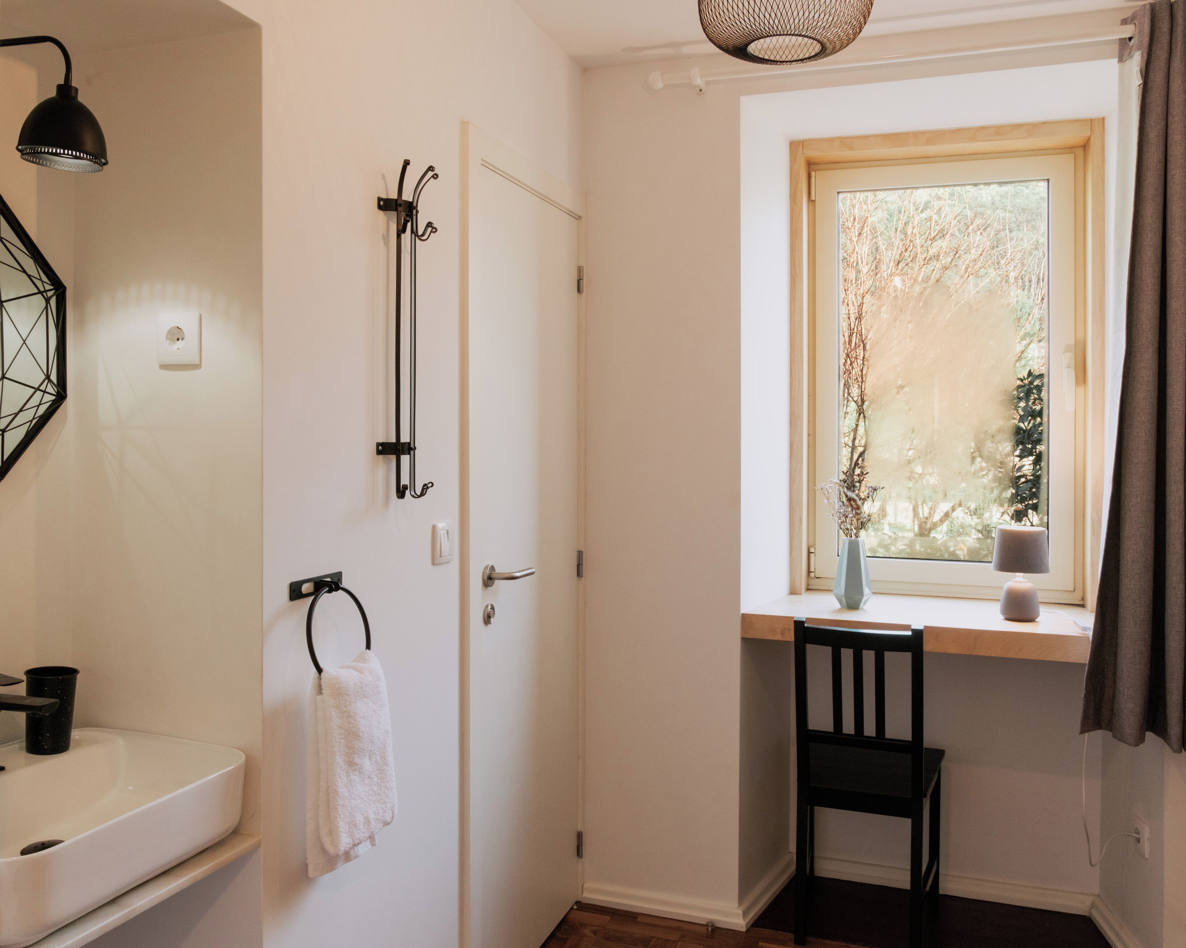Un baño con un lavamanos blanco, toallero y una ventana con vista a árboles.