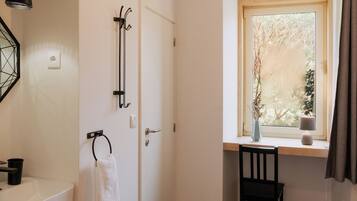 Un baño con un lavamanos blanco, toallero y una ventana con vista a árboles.