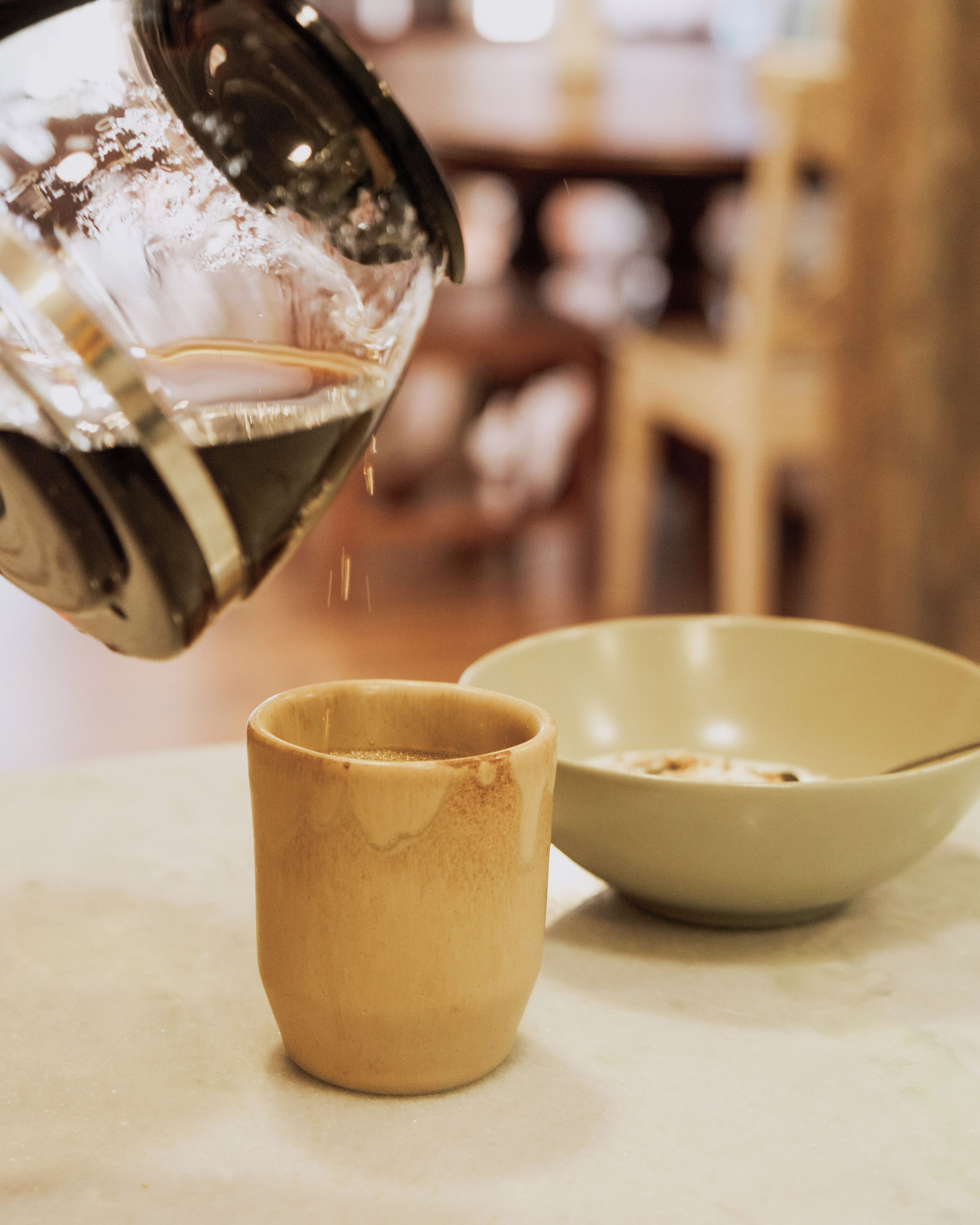 Una taza y un tazón de cerámica sobre una mesa, con un líquido que se vierte en la taza.