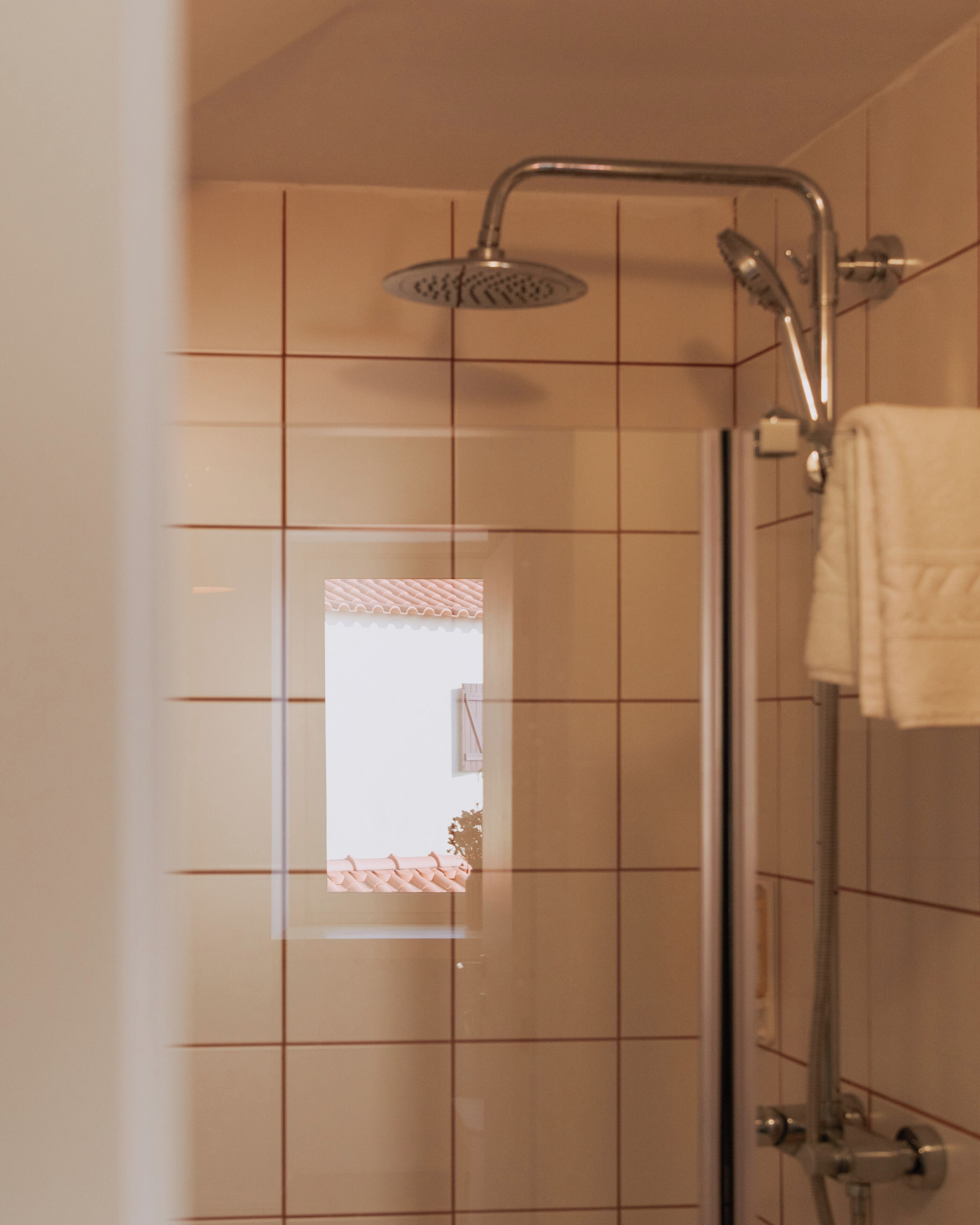 Un área de ducha con puerta de vidrio, paredes con azulejos y una toalla colgada en la pared.