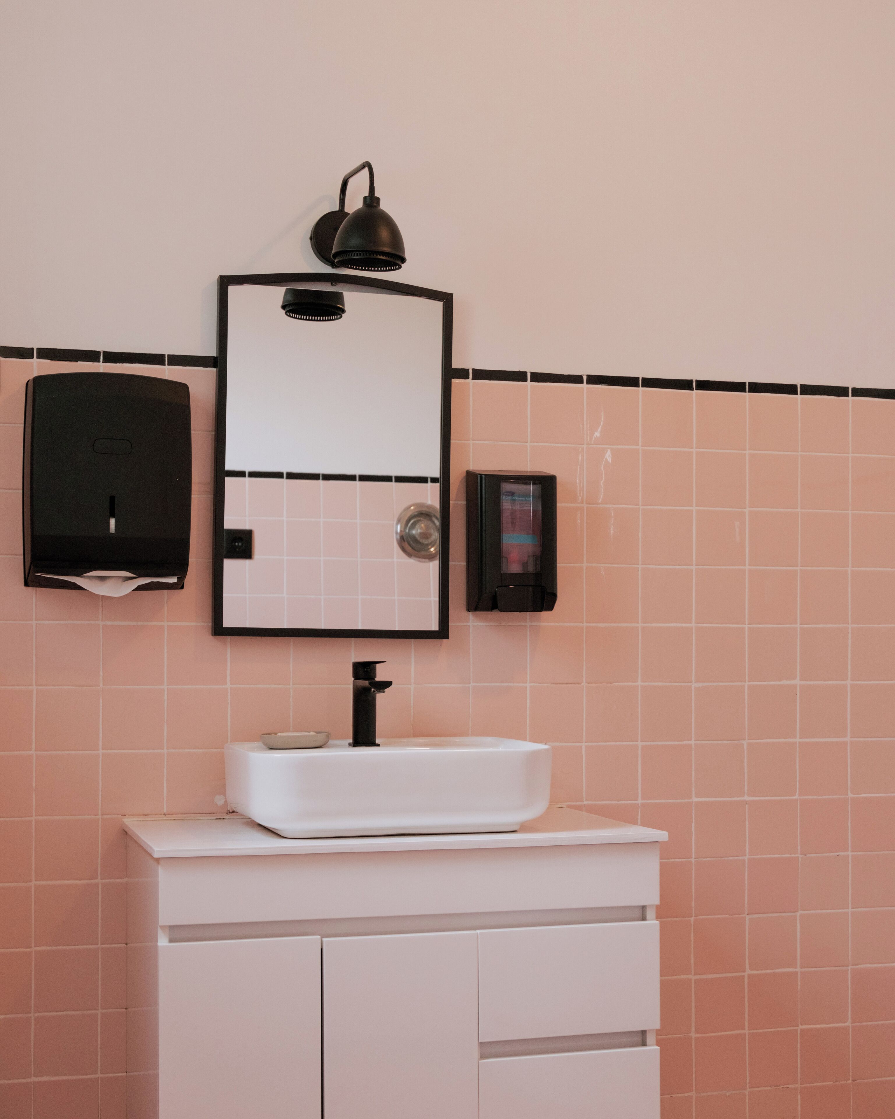 A bathroom with a white sink, a mirror, and a black wall-mounted light fixture.