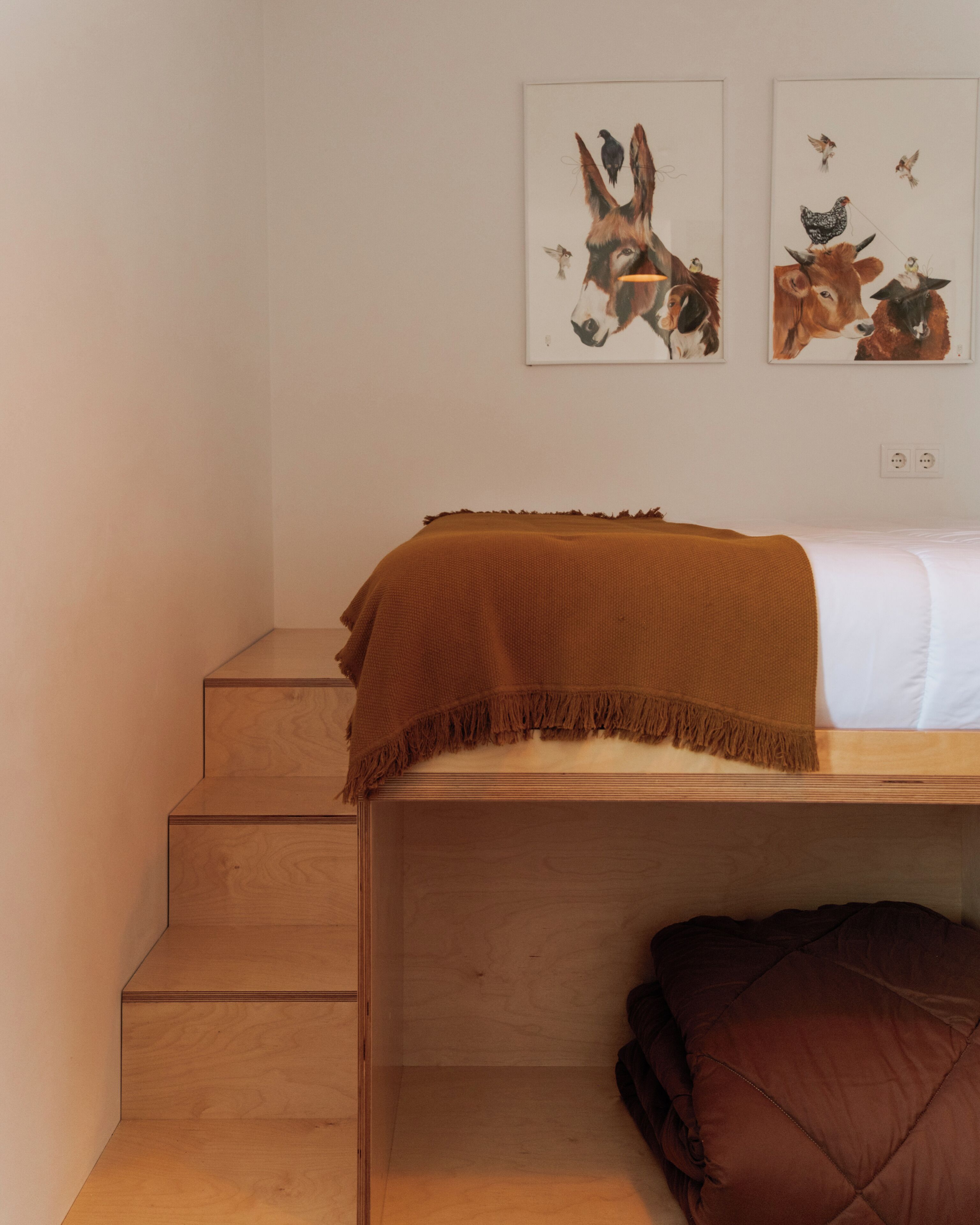 A bedroom with a wooden bed, a brown blanket, a pillow, and two wall-mounted paintings of animals.