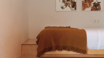 A bedroom with a wooden bed, a brown blanket, a pillow, and two wall-mounted paintings of animals.