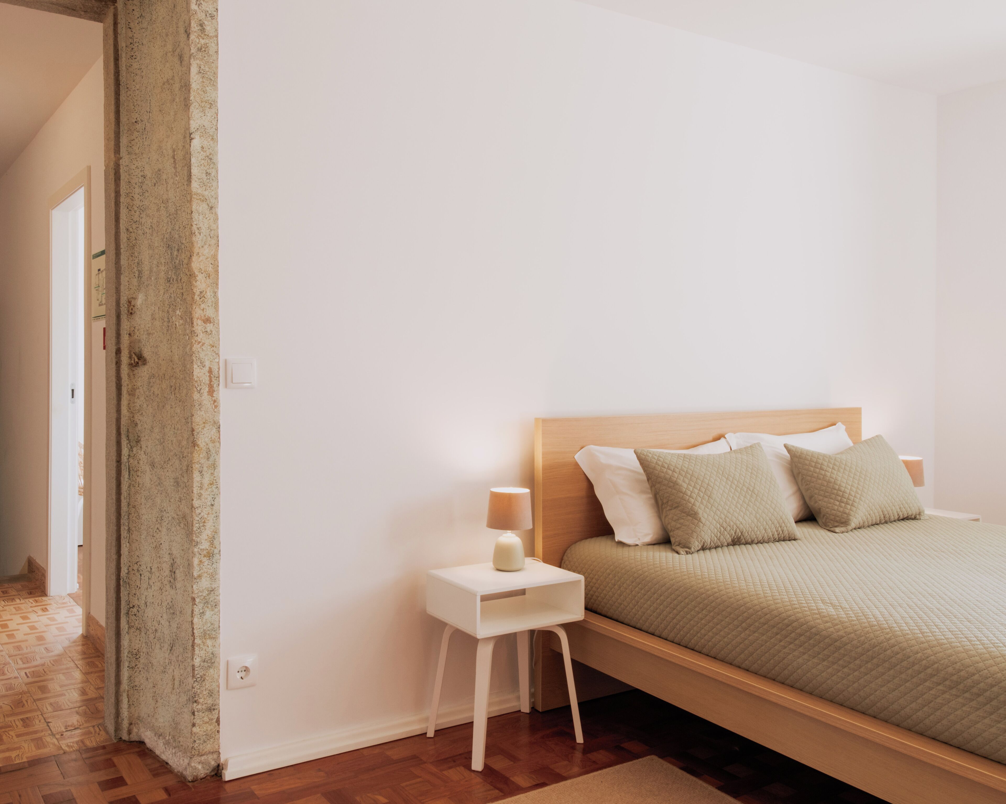 A bedroom with a wooden bed, white nightstand, and a small white table.