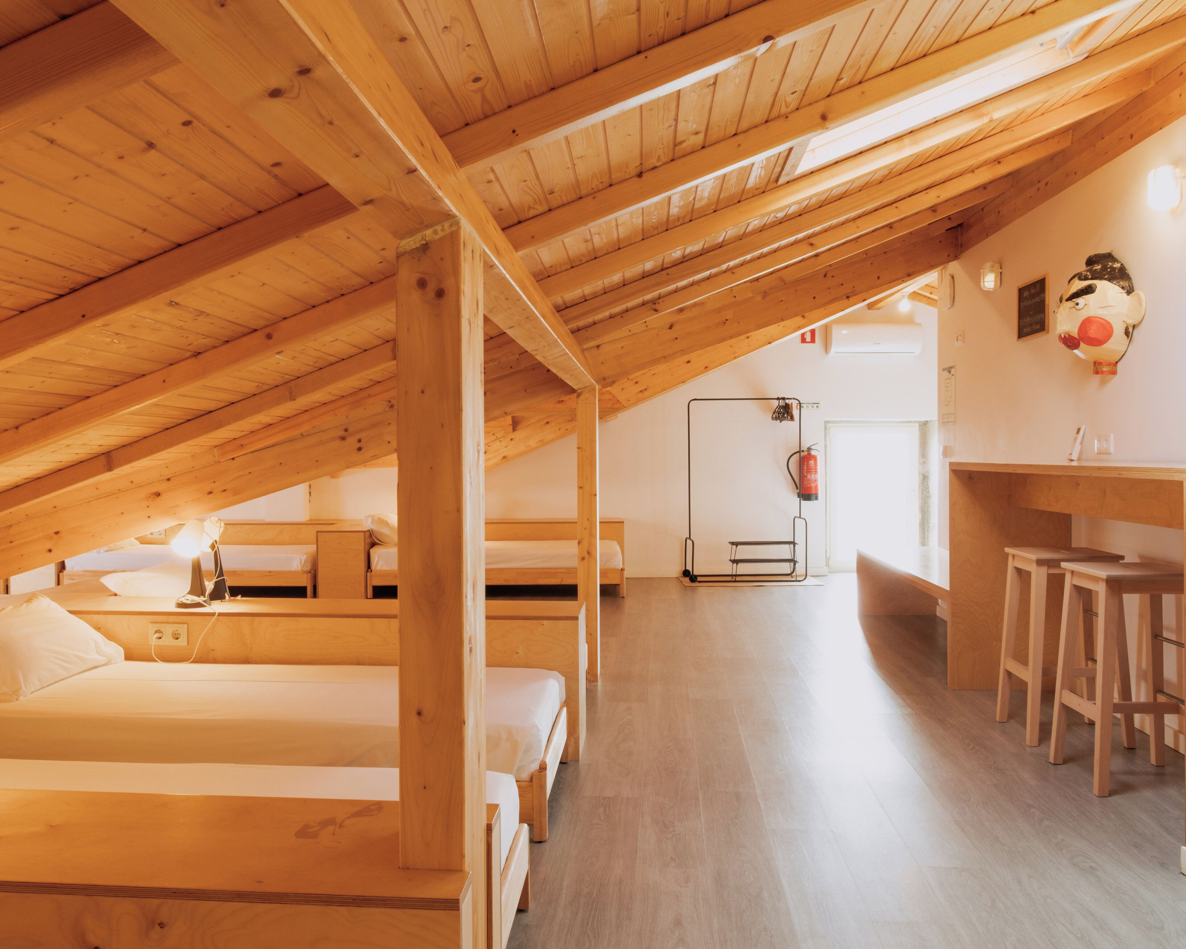 Un dormitorio acogedor en el ático con vigas de madera, literas, una pequeña kitchenette y un extintor.