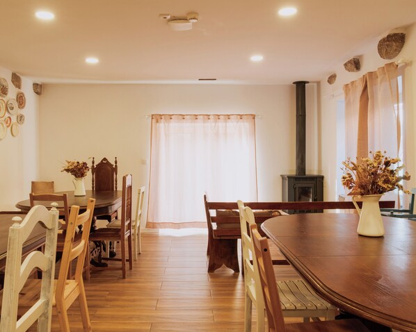 Une salle à manger avec une grande table en bois, des chaises, une cheminée et une fenêtre avec des rideaux.