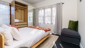 Ein Schlafzimmer mit Bett, Einbauschrank, Sitzecke und einem Fenster mit Vorhängen.