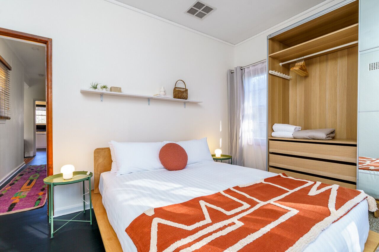 Een moderne hotelkamer met een groot bed, een houten garderobe, een klein tafeltje met een lamp en een plank met decoratieve objecten.