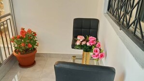 A corner of a room with a black chair, a potted plant with orange flowers, and a vase with pink flowers. - Appartement / Condominium de 3 Chambres et 3 Salles de Bain (Mamelles)
