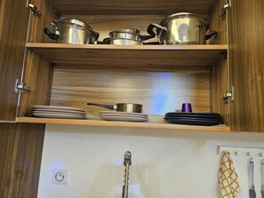 Una cocina con armarios de madera, ollas de acero inoxidable y una tetera.