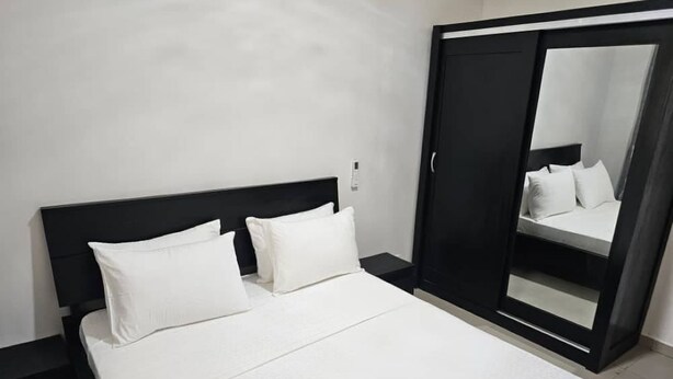 A neatly made bed with white linens and pillows, a black headboard, and a large mirror on the wall. - Appartement / Condominium de 3 Chambres et 3 Salles de Bain (Mamelles)
