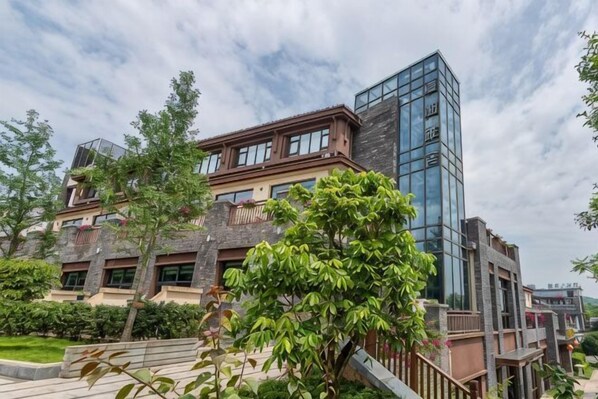 A multi-story building with a modern glass facade, surrounded by greenery and a paved walkway.