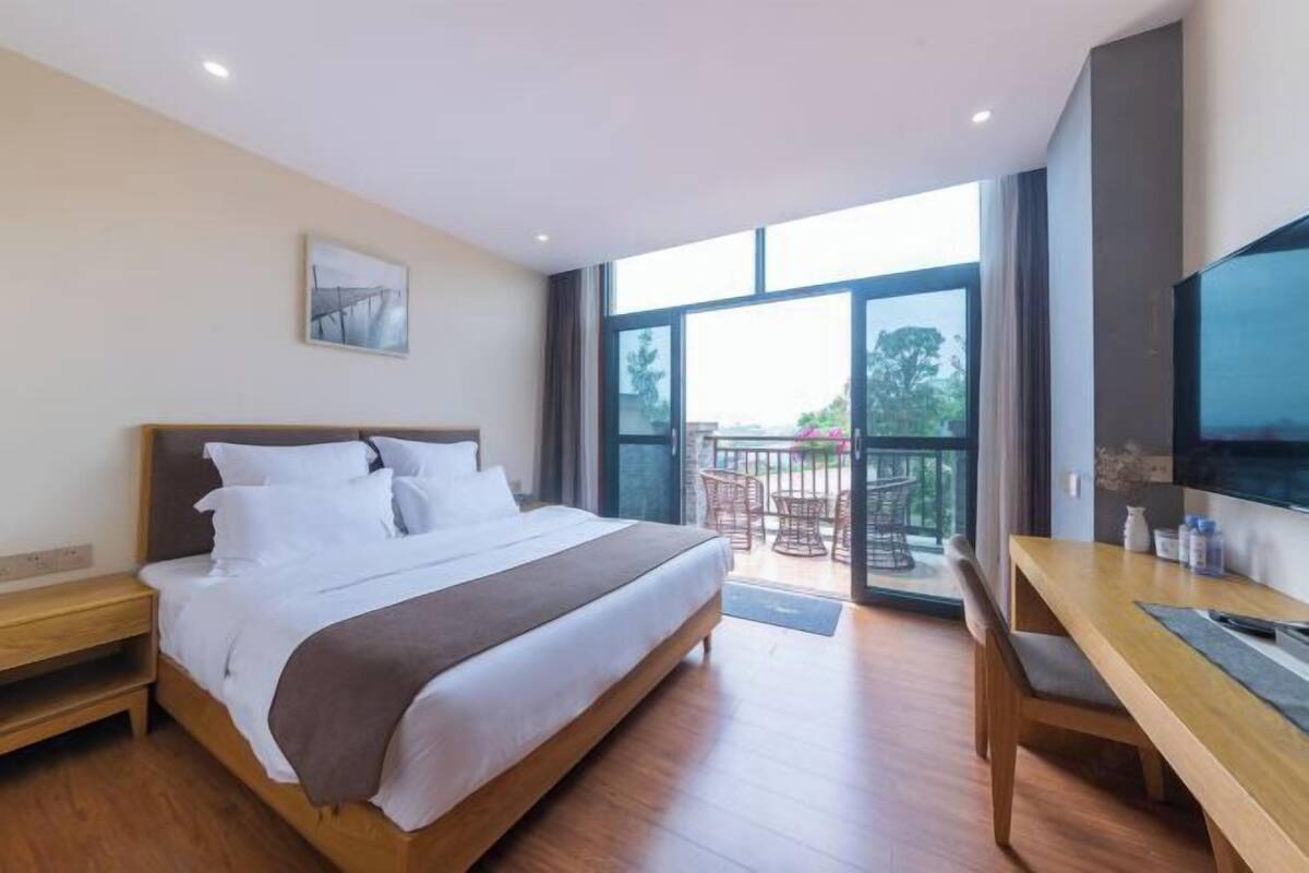 A bedroom with a bed, a desk, a TV, and a balcony with outdoor furniture.