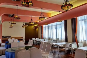 A dining area with round tables and chairs, overhead hanging lamps, and large windows with curtains. - Changshou Manhu Yashe Hotel (Chongqing)