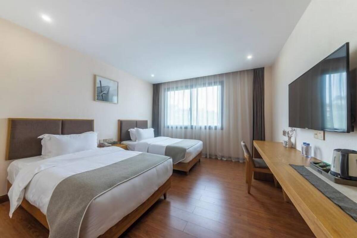 A hotel room with two beds, a TV, a desk, and a window with curtains.