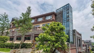 Edifício moderno com fachada de vidro e várias andares, cercado por vegetação e um gramado bem cuidado.