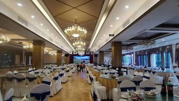 Un salón de banquetes con filas de mesas, sillas y un escenario central.