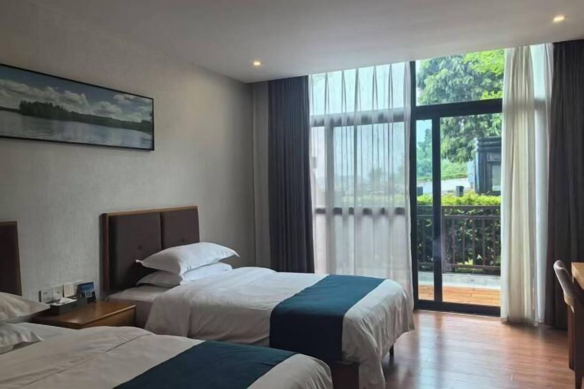 A hotel room with two beds, a painting on the wall, and a balcony with a view.
