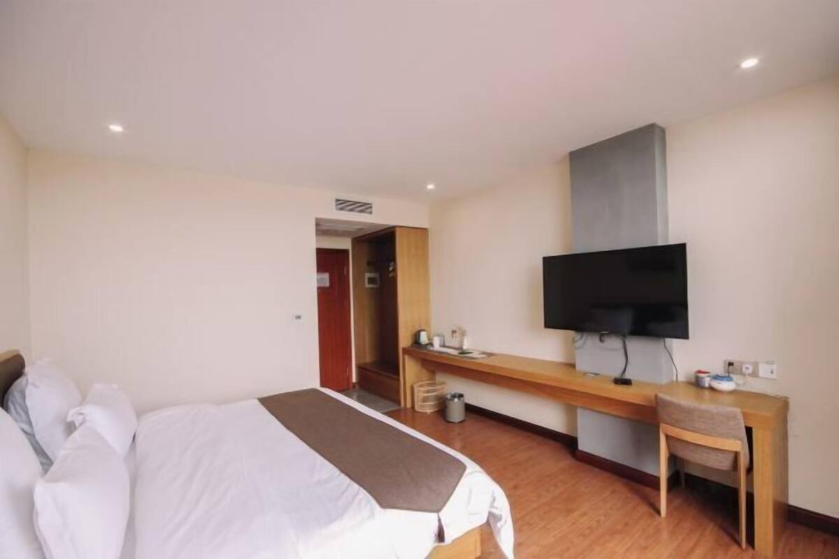 A hotel room with a bed, a desk, a television, and a shower area.