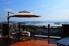 A terrace with a table and chairs, a large umbrella, and a view of a body of water. - Changshou Manhu Yashe Hotel (Chongqing)