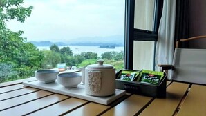 A table with a tray holding bowls and a container, near a window with a view of a lake and greenery. - Changshou Manhu Yashe Hotel (Chongqing)