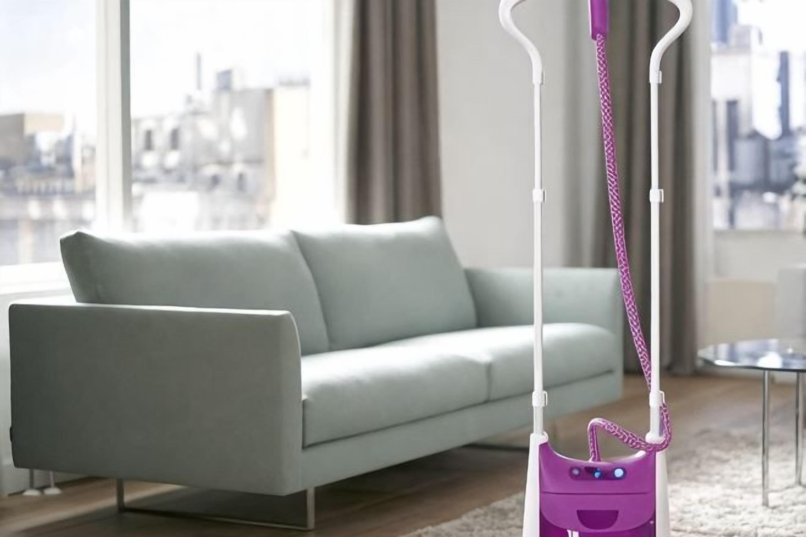 A modern living room with a light-colored sofa, a purple vacuum cleaner, and a view of a cityscape through large windows.