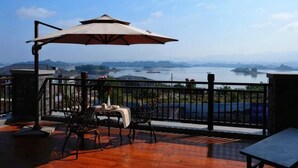 A terrace with a view of a body of water, a table, chairs, and an umbrella. - Changshou Manhu Yashe Hotel (Chongqing)