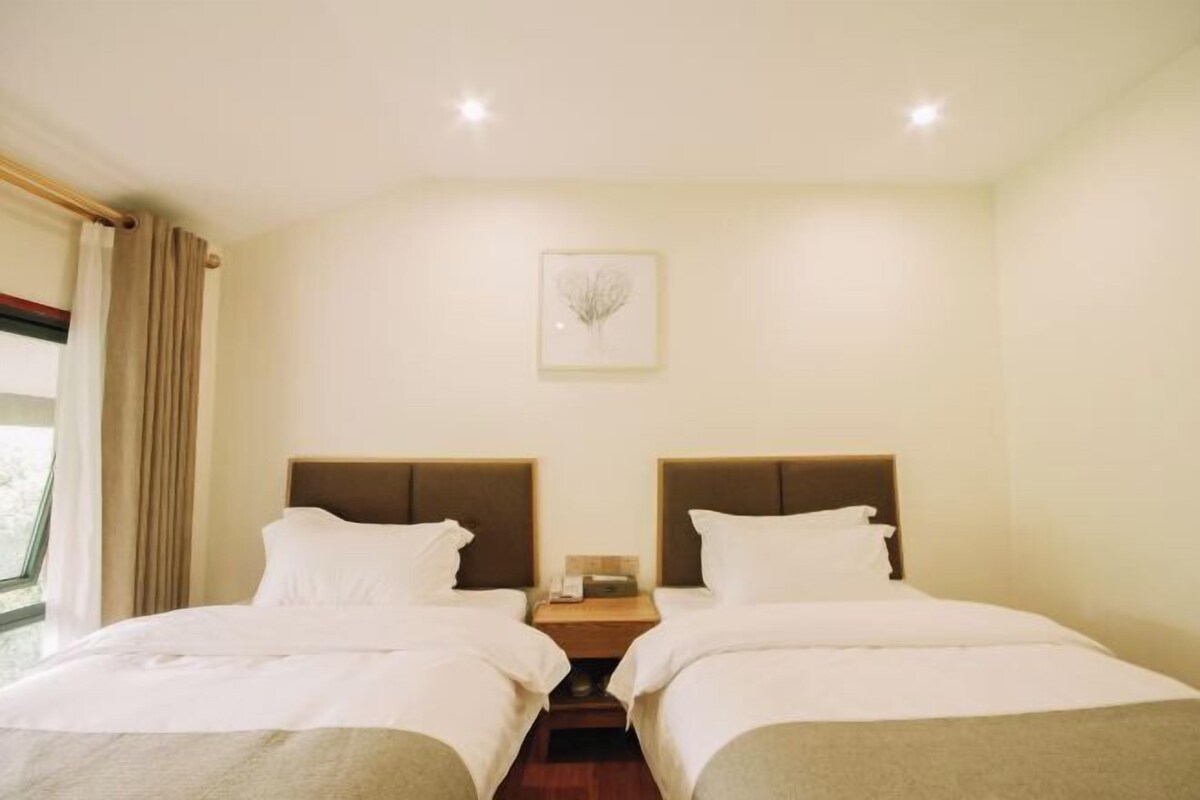 Habitación de hotel con dos camas, una mesita de noche, un cuadro enmarcado en la pared y una ventana con cortinas.