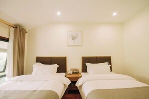 Habitación de hotel con dos camas, una mesita de noche, un cuadro enmarcado en la pared y una ventana con cortinas.
