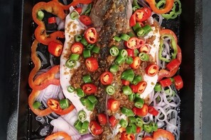 A fish with sliced red and green peppers and onions on a tray. - Changshou Manhu Yashe Hotel (Chongqing)