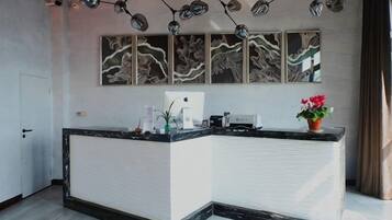 Un mostrador de recepción con encimera de mármol, una barra blanca y una planta en maceta. Se observan obras de arte en la pared y un colgador de techo.
