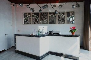 A reception desk with a marble top, a white counter, and a potted plant. There are wall-mounted artwork and a ceiling light fixture. - Changshou Manhu Yashe Hotel (Chongqing)