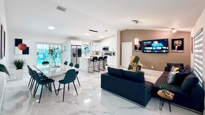 A modern living room with a sofa, a dining area with a glass table, and a kitchen in the background. - Miami house, Heated pool, Artificial beach, Mini golf, luxury and comfort (MIAMI)
