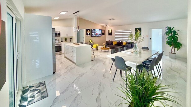 A modern kitchen with white cabinets, a dining area with a marble table, and a living room with a sofa and TV. - Miami house, Heated pool, Artificial beach, Mini golf, luxury and comfort (MIAMI)