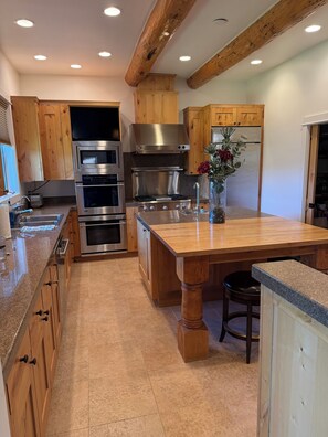 A kitchen with wooden cabinets, stainless steel appliances, a granite countertop, and a central island with stools.