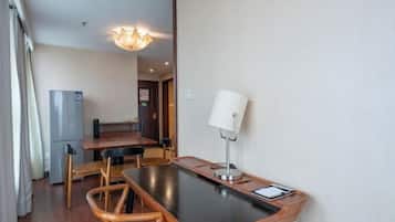 Una habitación compacta con una mesa de comedor, sillas, lámpara, refrigerador y una puerta que da a otra habitación.