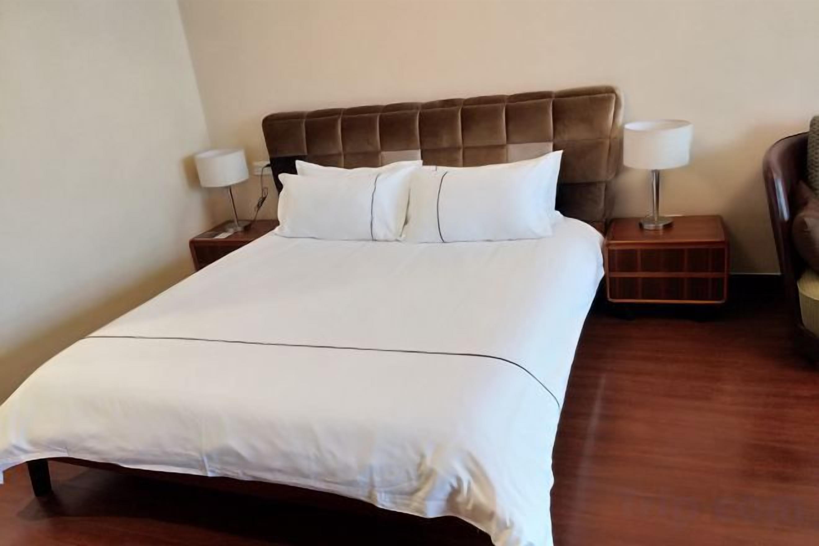 A neatly made bed with a headboard, two bedside tables with lamps, and a chair.