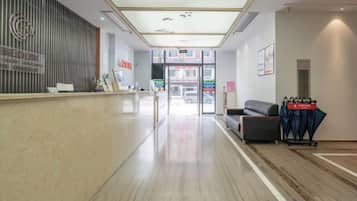 Uma área de recepção de hotel, com balcão de atendimento, sala de espera com sofá e vista para a rua.
