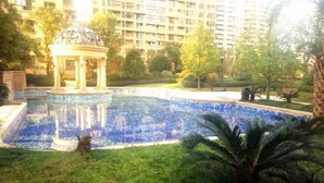 A swimming pool with a gazebo, surrounded by greenery and a high-rise building in the background. - Bedom Apartment (Hengdian Nanjiang No. 1 Branch) (Dongyang)
