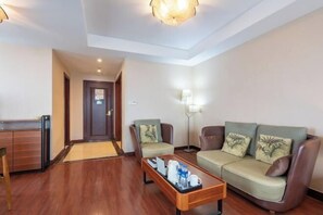 A hotel room with a wooden floor, a sofa, two armchairs, a coffee table with a tray, a lamp, and a door. - Bedom Apartment (Hengdian Nanjiang No. 1 Branch) (Dongyang)