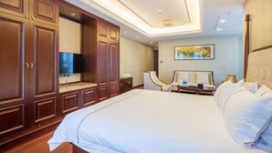A hotel room with a large bed, wooden wardrobe, a flat-screen TV, a desk with a chair, and a painting on the wall. - Bedom Apartment (Hengdian Nanjiang No. 1 Branch) (Dongyang)