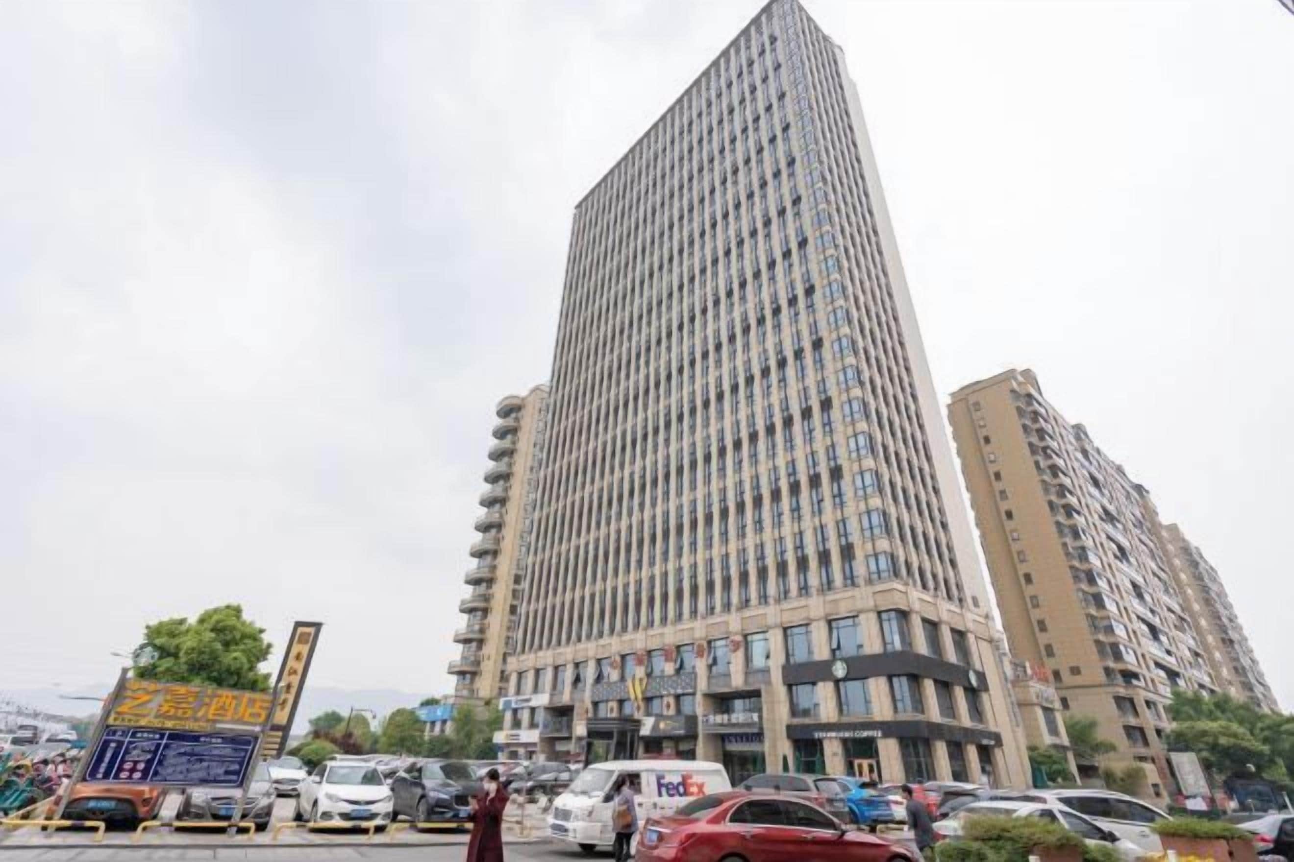 A tall, modern building with a grid-like facade, surrounded by other buildings and parked cars.